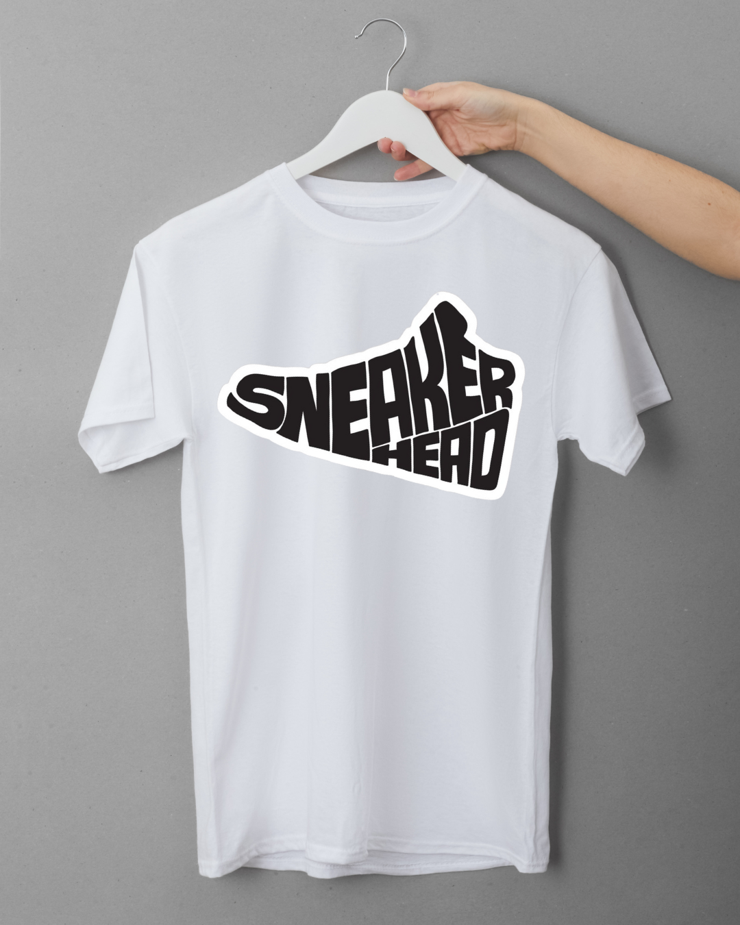 White t-shirt with 'SNEAKERHEAD' graphic on a hanger against a gray background