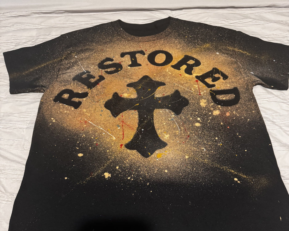Black t-shirt with 'RESTORED' text and cross design on a textured surface