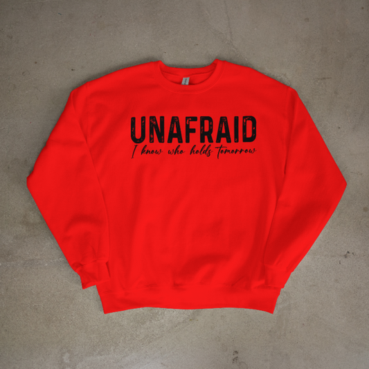 Red sweatshirt with 'UNAFRAID I know who holds tomorrow' text on a gray surface