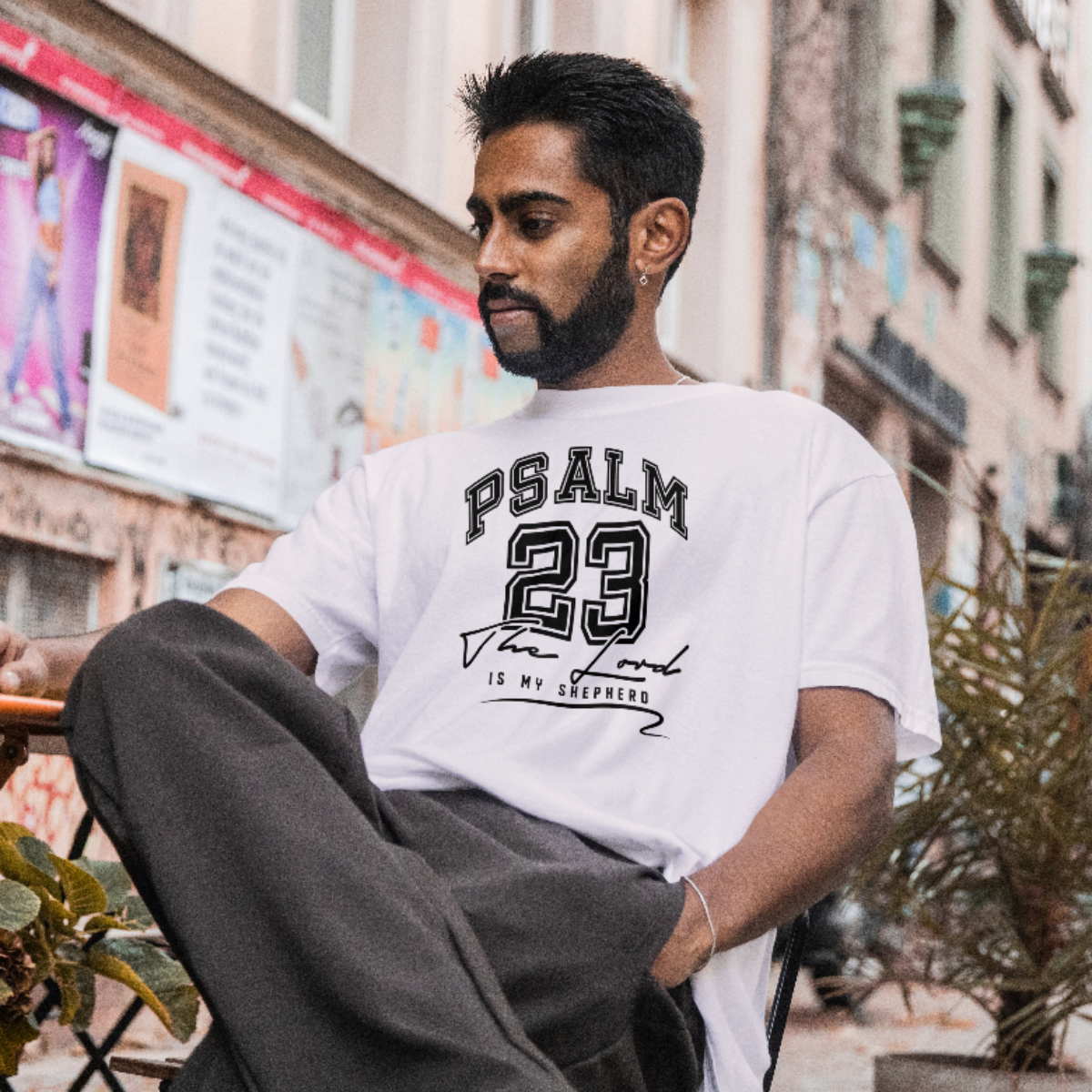Man wearing a white t-shirt with 'PSALM 23' text sitting outdoors.