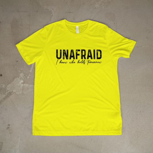 Yellow t-shirt with 'UNAFRAID I know who holds tomorrow' text on a concrete floor.