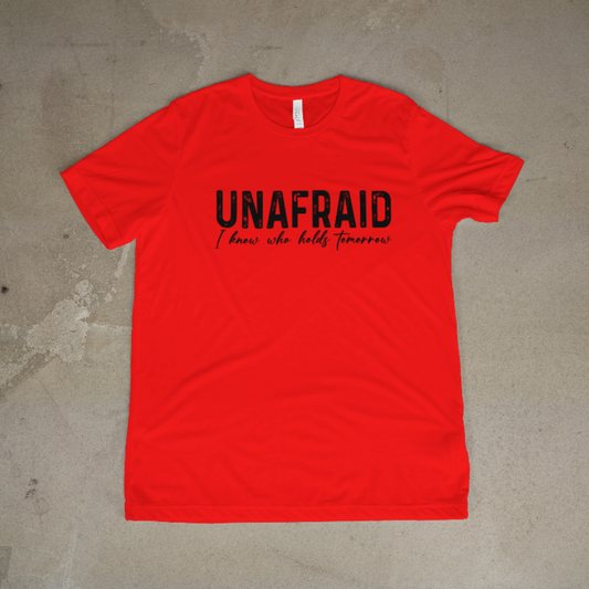 Red t-shirt with 'UNAFRAID I know who holds tomorrow' text on a concrete floor.