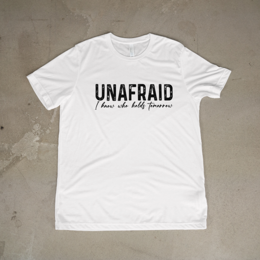 White t-shirt with 'UNAFRAID I know who holds tomorrow' text on a concrete surface