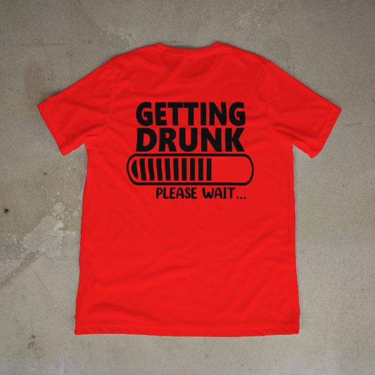 Red unisex t-shirt with ‘Getting Drunk… Please Wait Loading’ graphic, flat lay on beige background, short sleeve casual tee