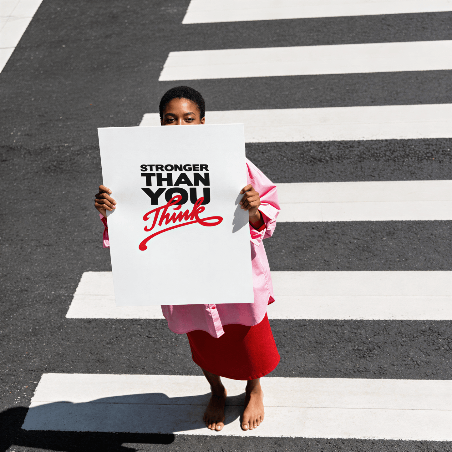 Person holding a sign with 'Stronger Than You Think' on a crosswalk