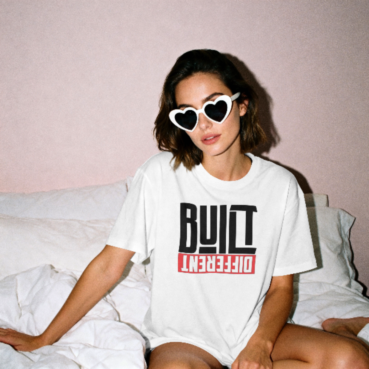 Person wearing a white t-shirt with text, sitting on a bed.