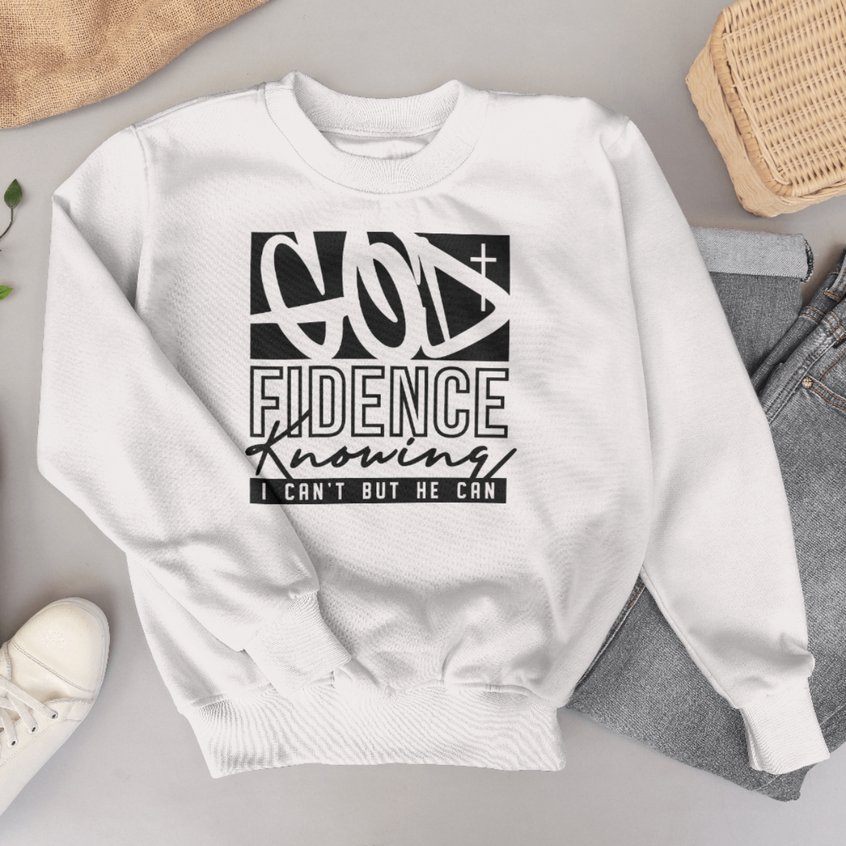 White sweatshirt with black text design on a gray surface with shoes and jeans.