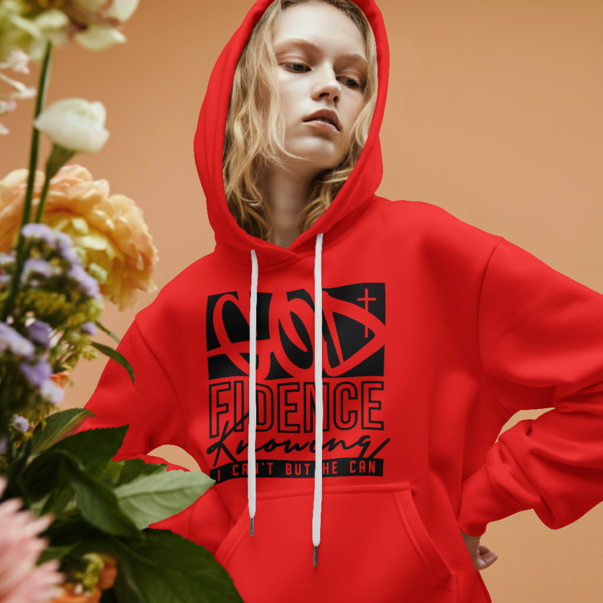 Person wearing a red hoodie with text, holding flowers against a beige background