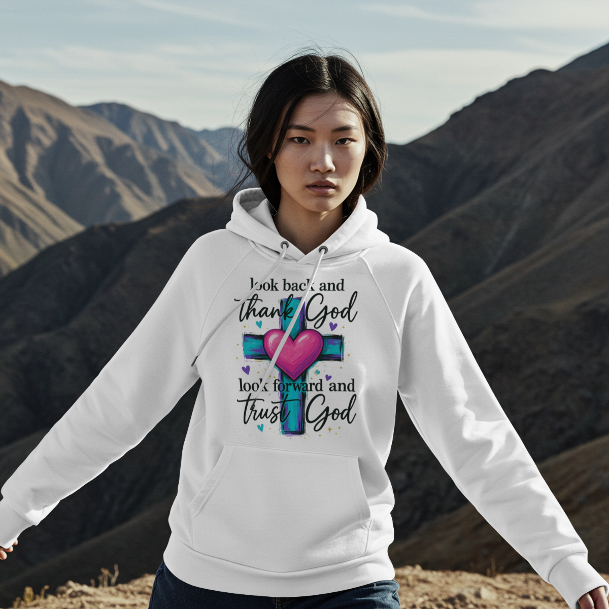 Person wearing a white hoodie with a motivational quote and colorful design, standing against a mountainous landscape.