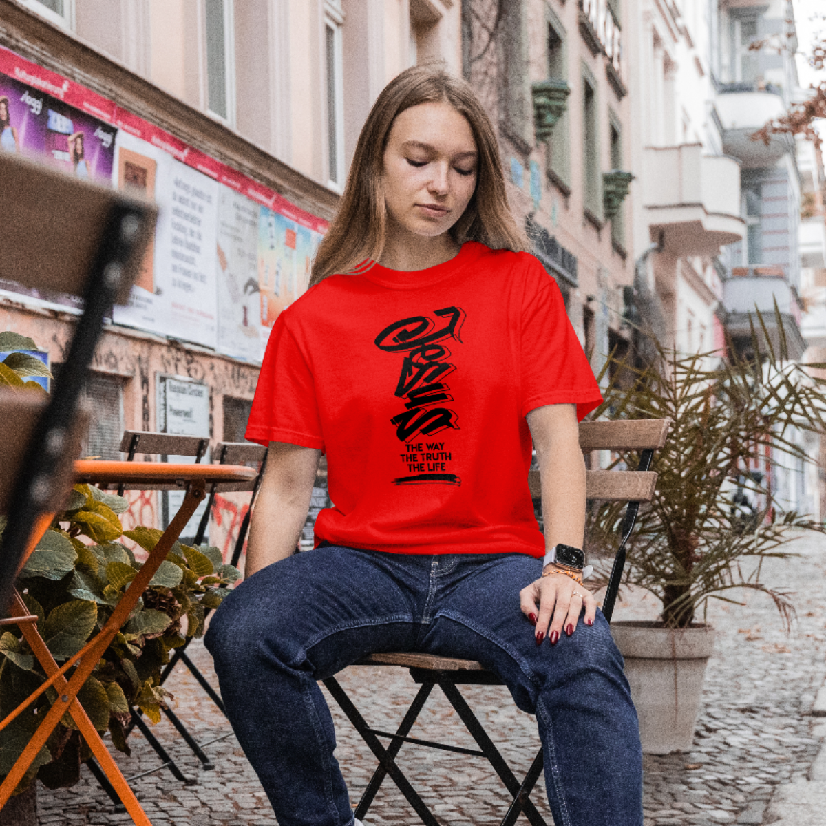 Woman wearing a red t-shirt with black text sitting on a chair in an urban setting.