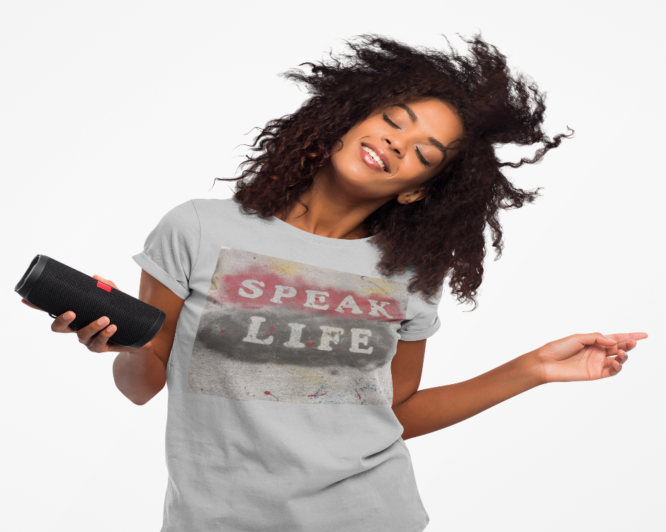 Woman wearing a 'Speak Life' t-shirt holding a black speaker against a white background