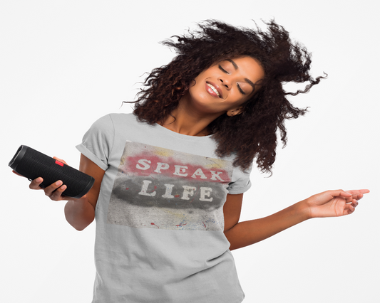Woman wearing a 'Speak Life' t-shirt holding a black speaker against a white background