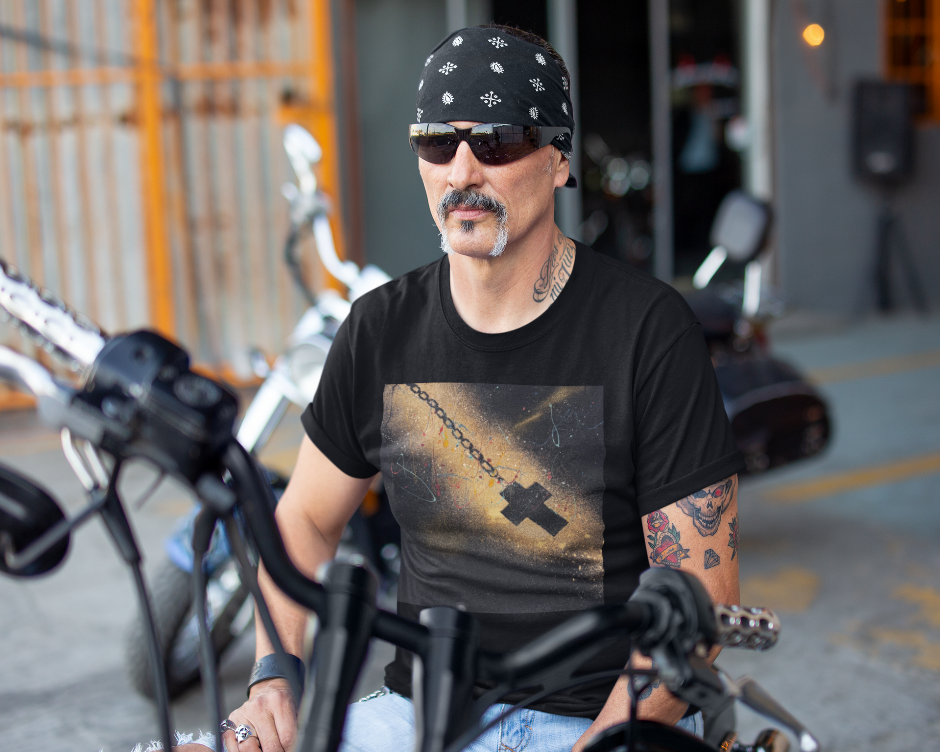 Man wearing a black t-shirt with a graphic design, sunglasses, and a bandana sitting on a motorcycle.